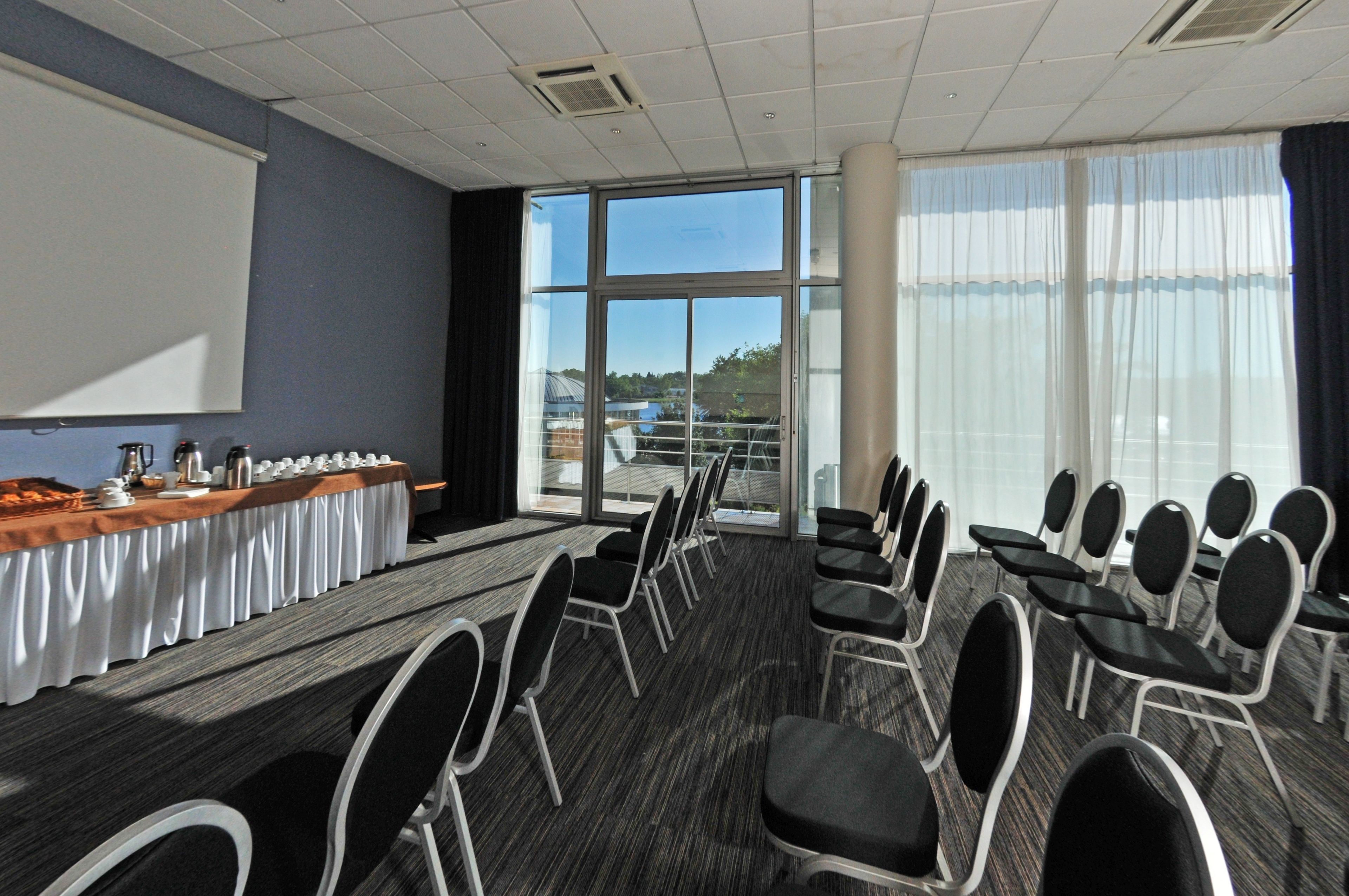 A conference room with a long table, chairs, a projector screen, and large windows.