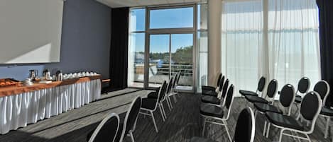 A conference room with a long table, chairs, a projector screen, and large windows.