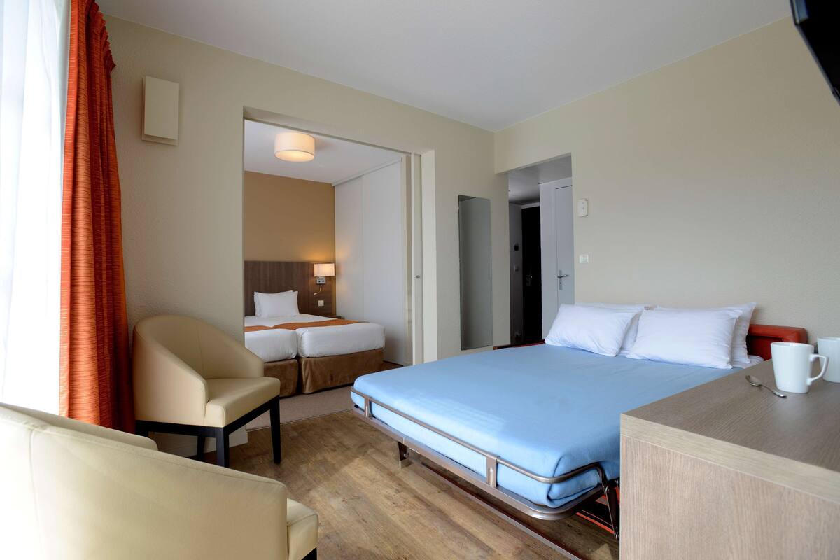 A hotel room with a bed, a chair, a desk, and a small table.