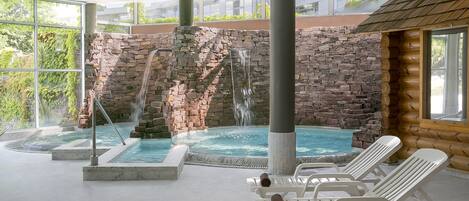 Un área de spa con cascada de piedra, bañera de hidromasaje y sillones de descanso.