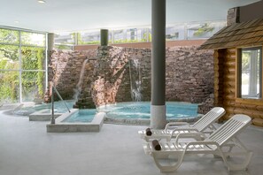 Un área de spa con cascada de piedra, bañera de hidromasaje y sillones de descanso.