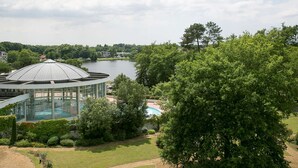 A glass-domed structure with a pool, surrounded by lush greenery and a lake. - Best Western Sourceo (Saint-Paul-les-Dax)