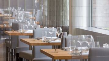 A restaurant with multiple tables set for dining, featuring a modern interior with glass partitions and large windows.