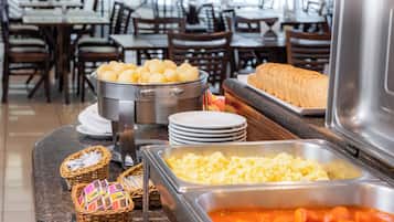 A buffet setup with various food items, including a pot of potatoes, a tray of bread, and a container of scrambled eggs.