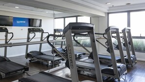 Ein Fitnessraum mit Laufbändern, einer Spiegelwand und einem Fernseher.