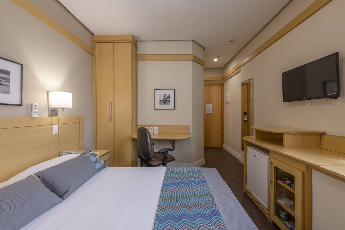 Una habitación de hotel con cama, escritorio, silla, televisor y refrigerador pequeño.