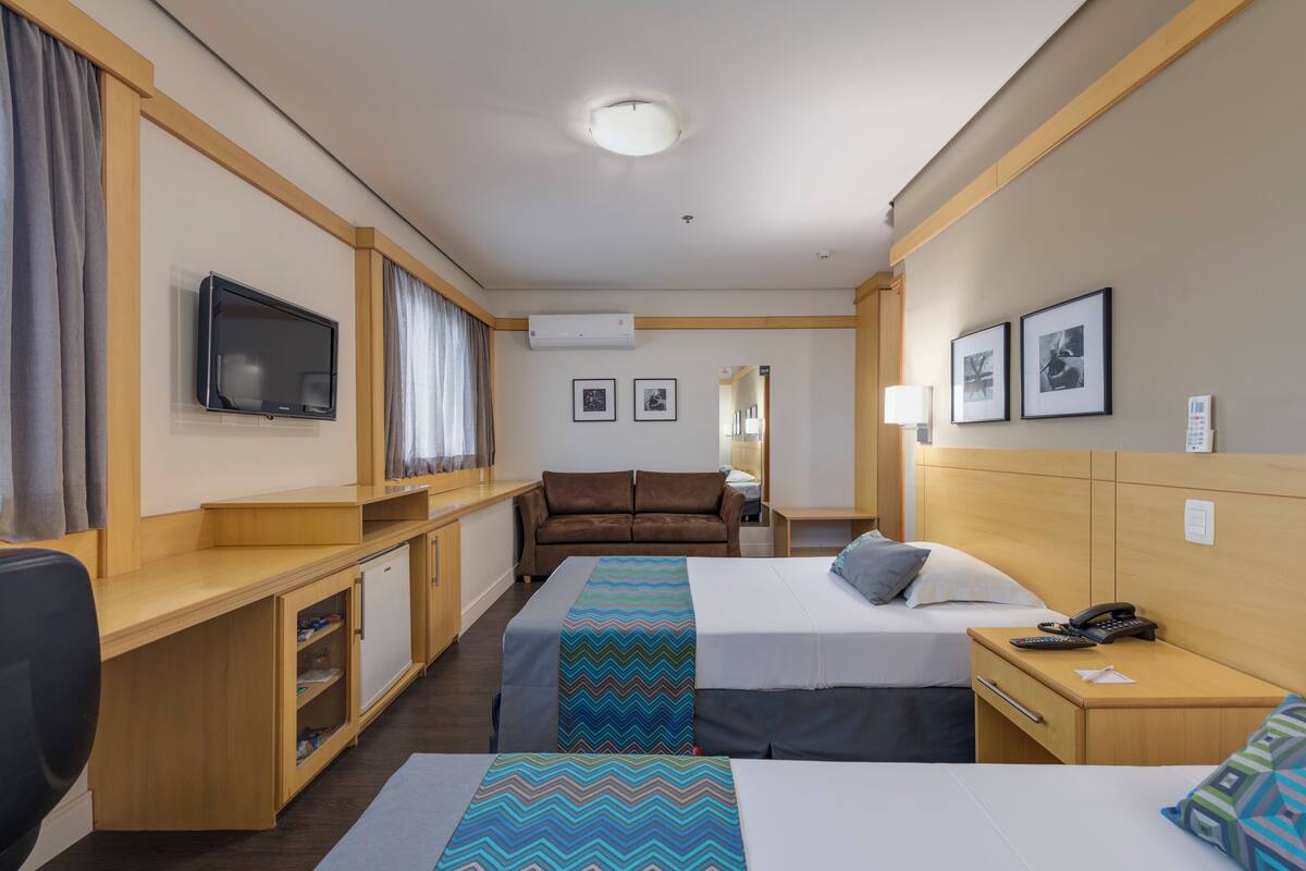 Una habitación de hotel con dos camas, un escritorio, un televisor, un sofá y un espejo.