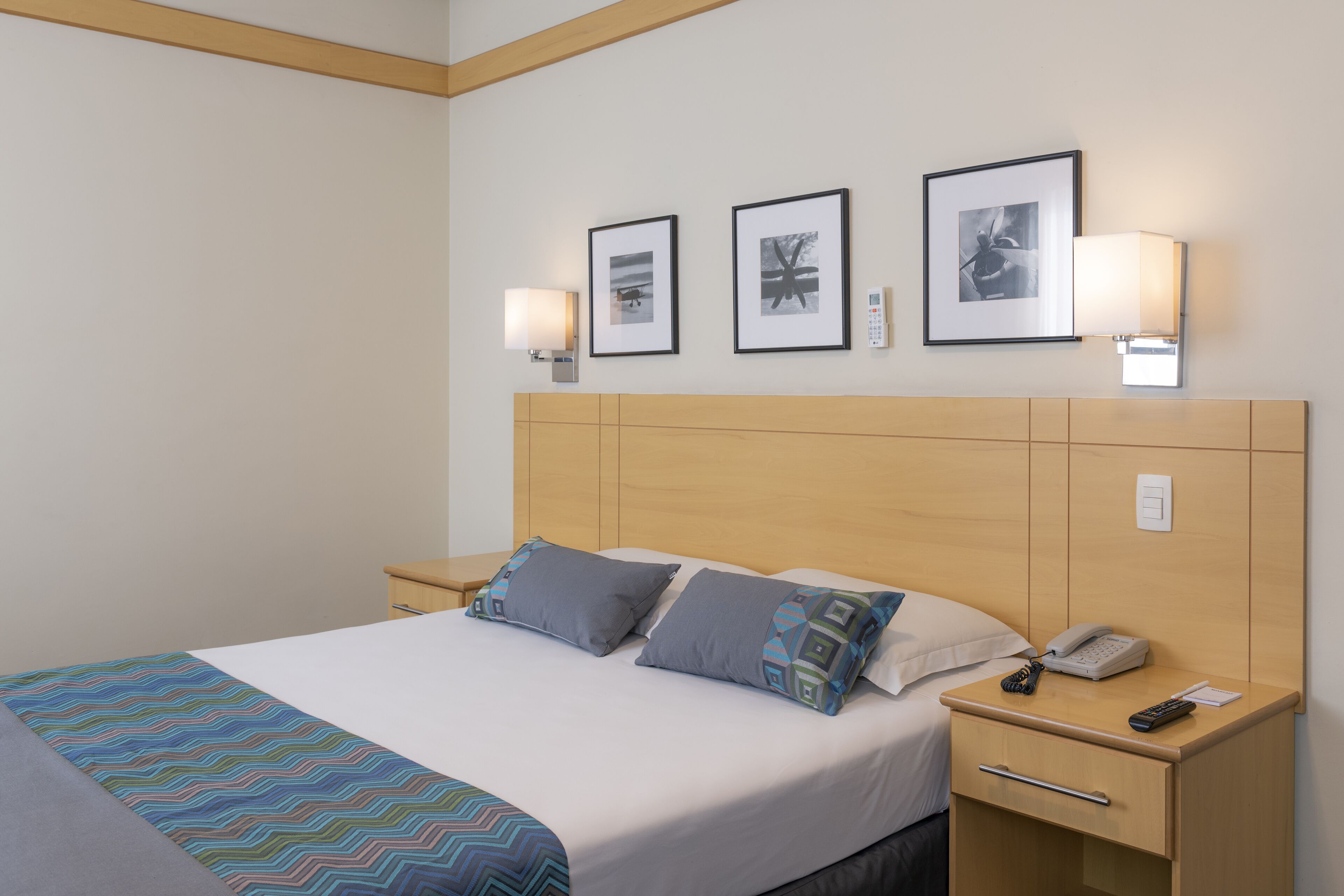 A hotel room with a bed, bedside tables, a nightstand, and wall-mounted lamps.