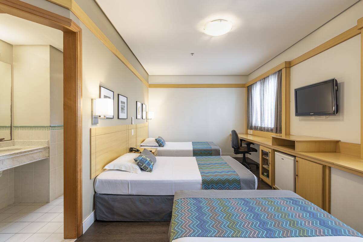 Habitación de hotel con dos camas, un escritorio, un televisor y una kitchenette pequeña.