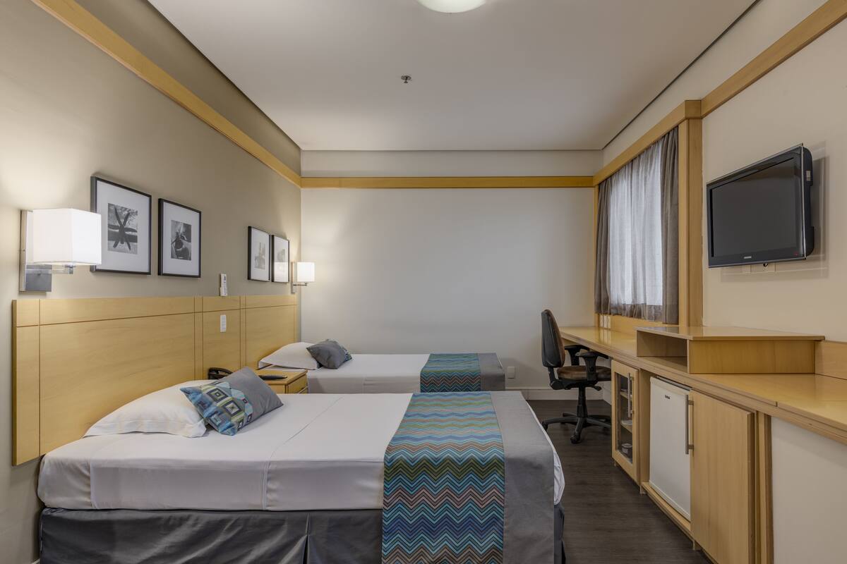 Habitación de hotel con dos camas, un escritorio, televisor y cuadros en la pared.