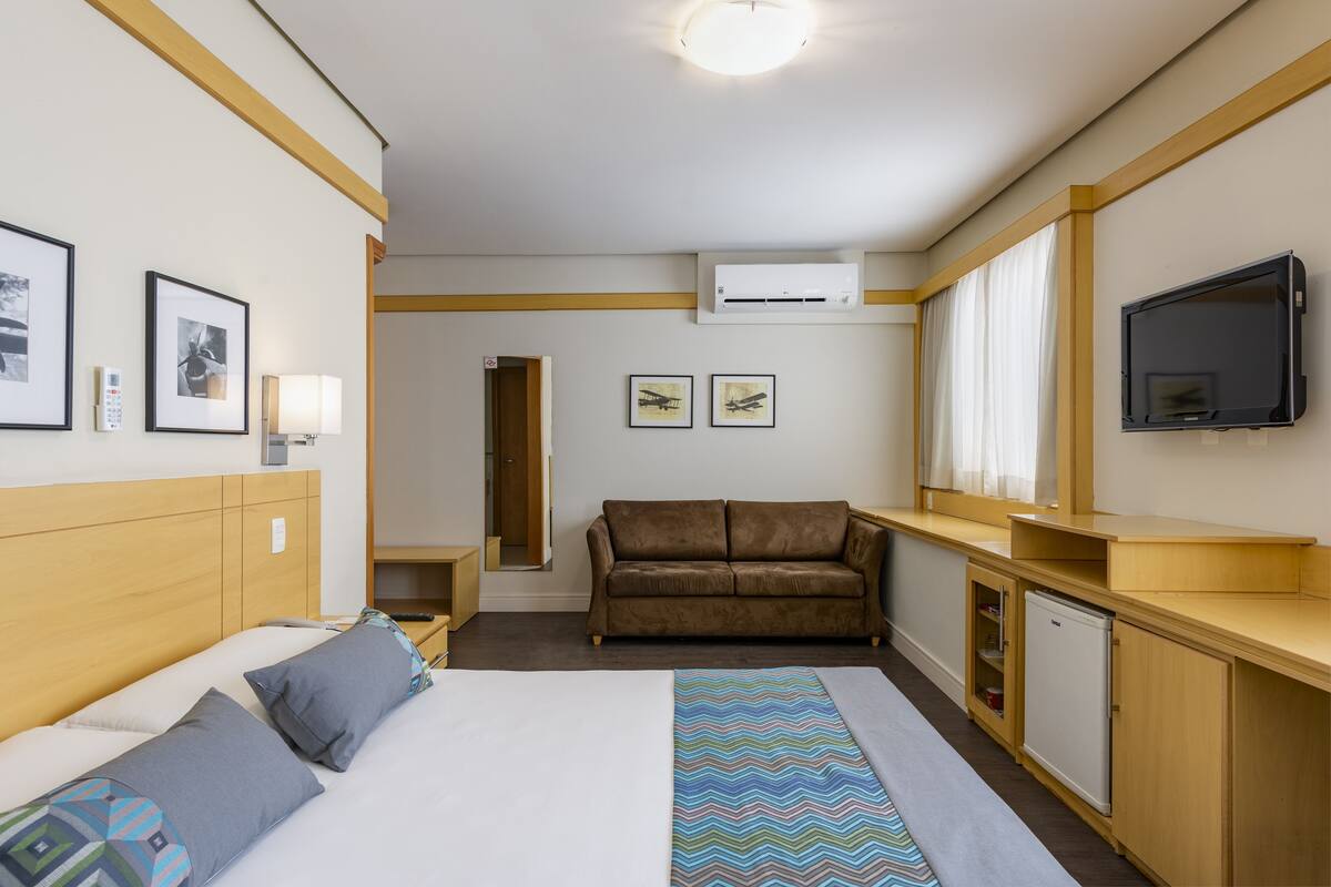 Una habitación de hotel con cama, sofá, televisor y escritorio.