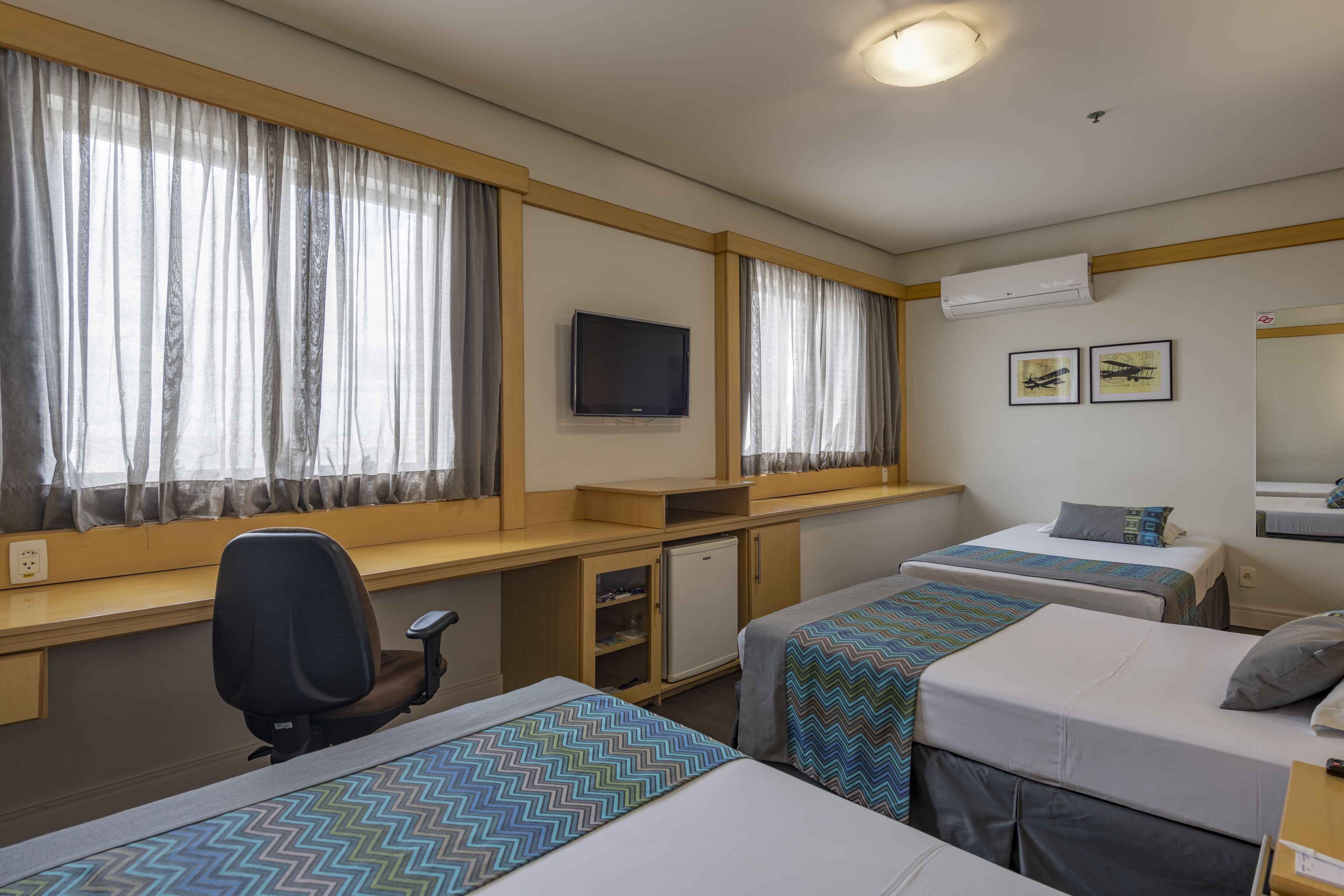 Habitación de hotel con dos camas individuales, un escritorio con silla, televisor y aire acondicionado.