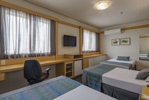 Habitación de hotel con dos camas individuales, un escritorio con silla, televisor y aire acondicionado.