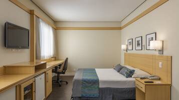 Una habitación de hotel con una cama, un escritorio, una silla, un televisor y una mesita de noche con lámpara.