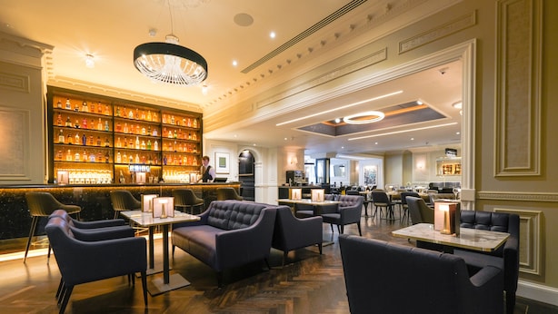 Angolo bar con ampia esposizione di vino e liquori, sedute confortevoli e un lampadario.