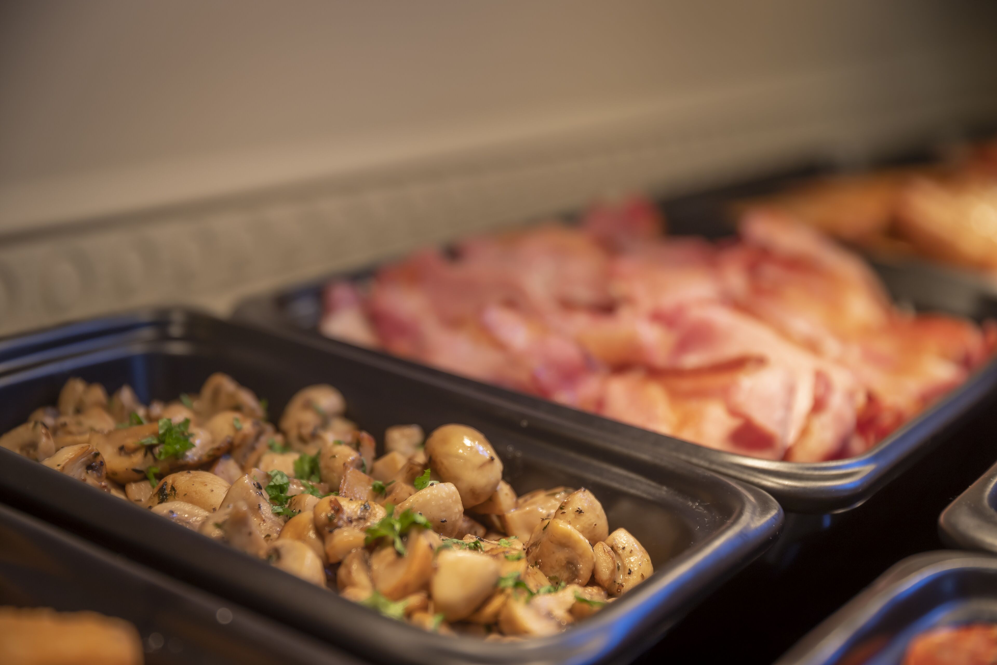 Un bufé con diversas opciones de comida, incluyendo setas en rodajas y jamón.