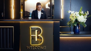 Una reception con un logo a forma di 'B' e la scritta 'WELCOME', un'addetta alla reception e un vaso di fiori.
