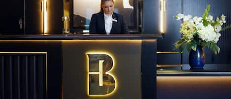 En receptionsdisk med en logotyp i form av bokstaven ”B” och texten ”VÄLKOMMEN”, en receptionist och en vas med blommor.