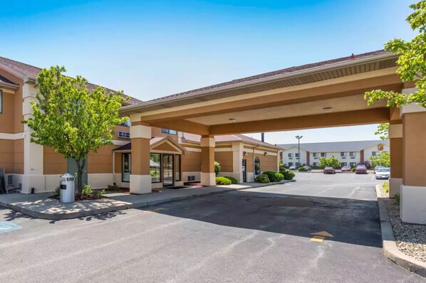 A hotel entrance with a covered driveway, a parking lot, and a building with a beige facade.