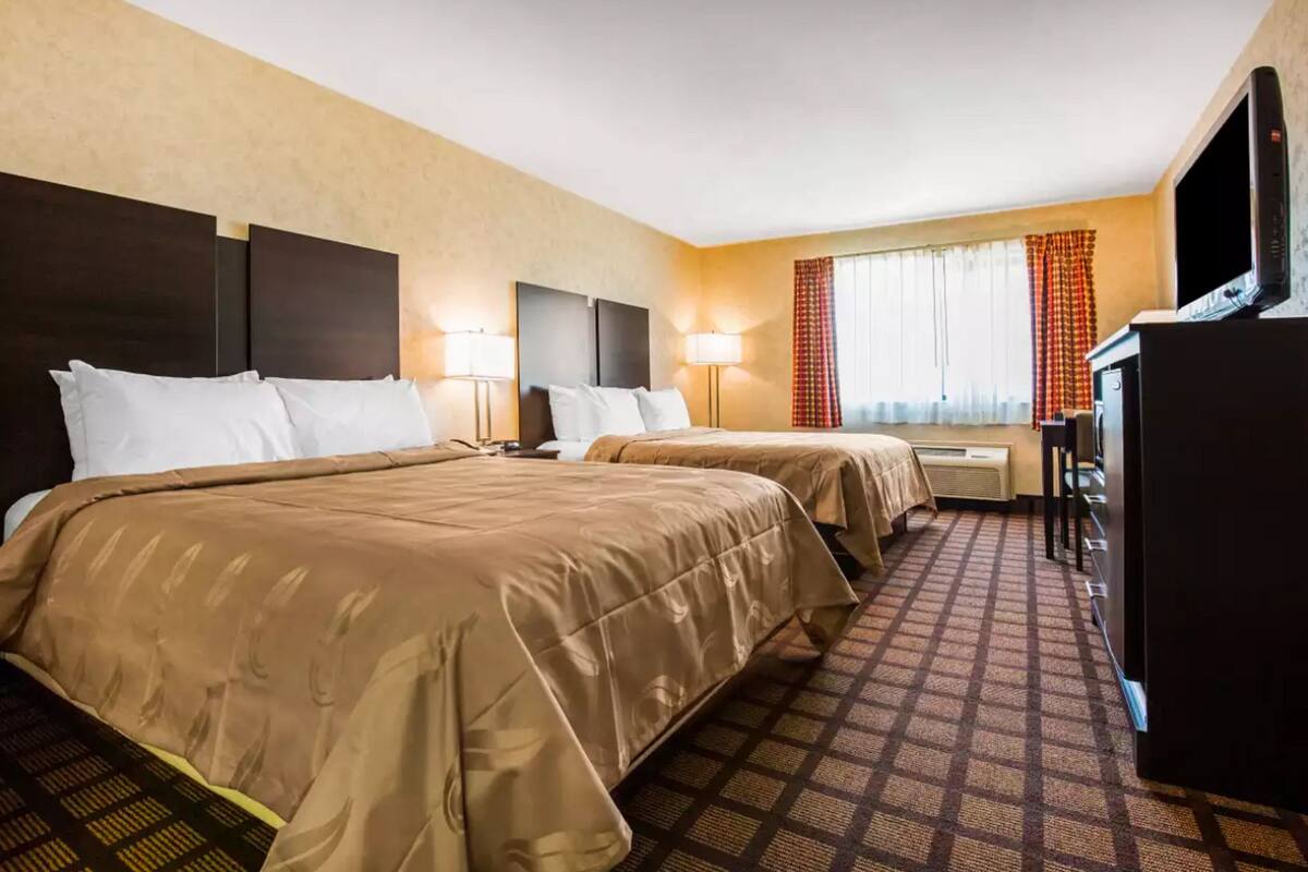 A hotel room with two beds, a TV, and a desk.