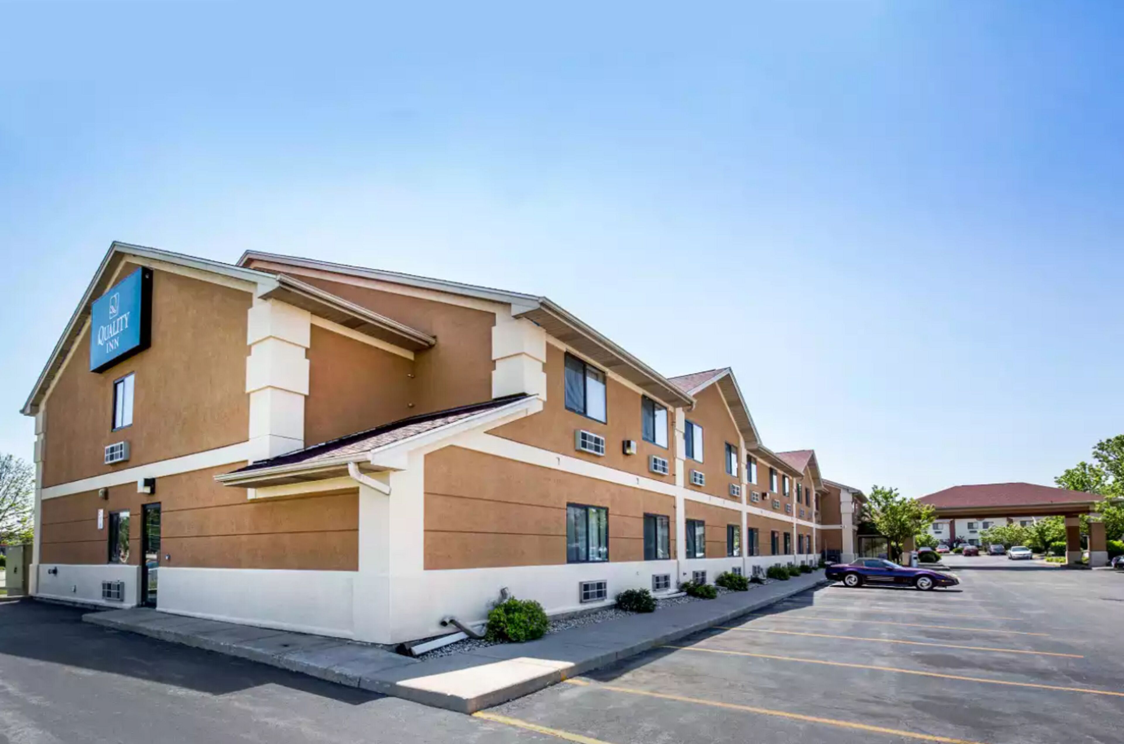 A hotel with a brown and beige exterior, multiple windows, and a parking lot with a few cars.