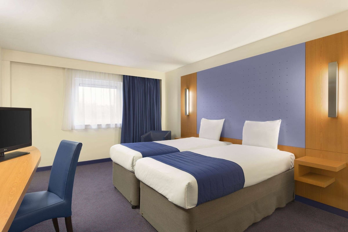 A hotel room with two beds, a desk, a chair, and a television.
