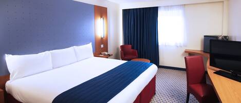 A hotel room with a large bed, a desk, a TV, and a chair.