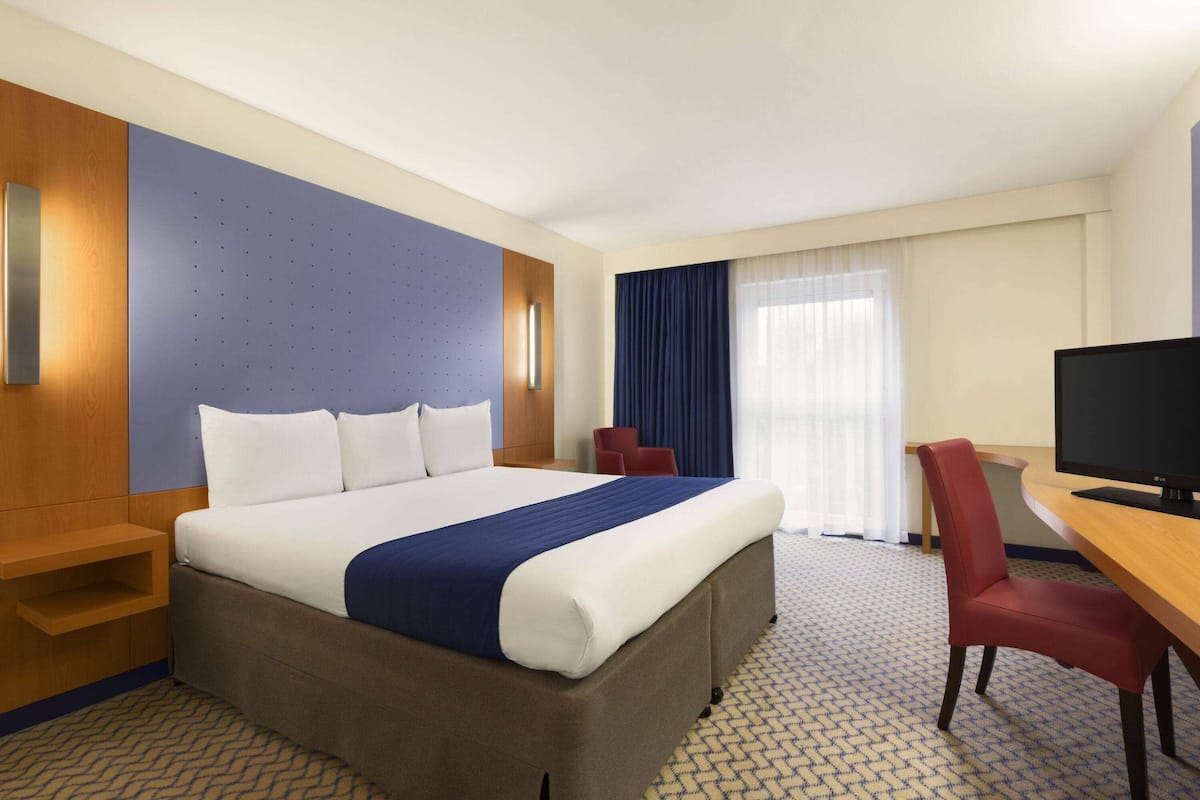 A hotel room with a large bed, a desk with a television, a red chair, and a window with curtains.