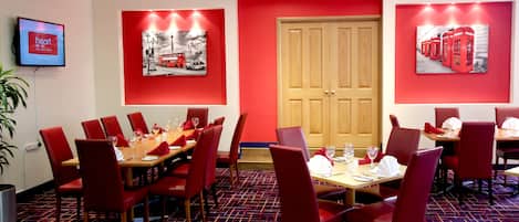 A dining area with red chairs and tables, a wooden door, and two red-framed pictures on the walls.