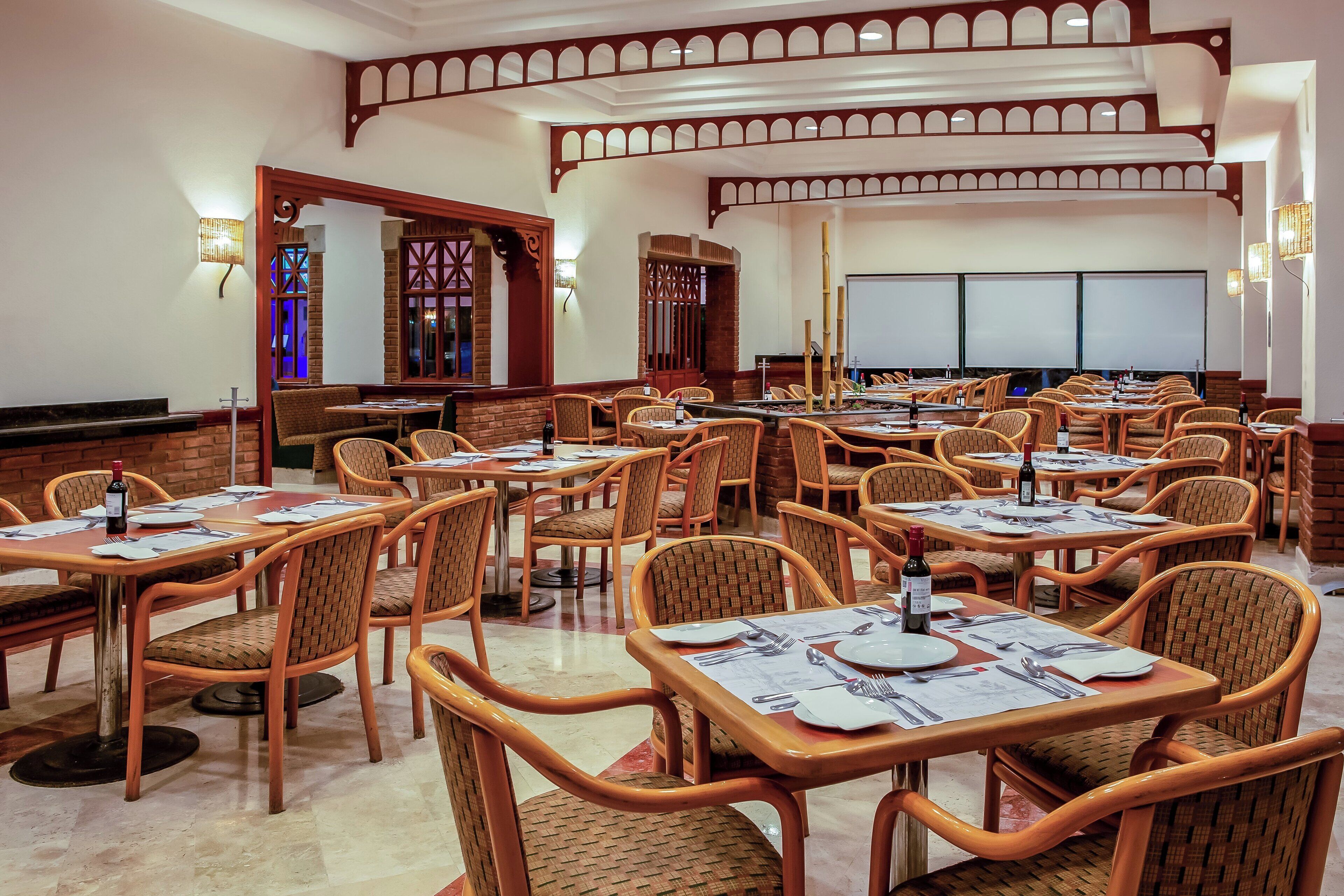 Restaurante com várias mesas e cadeiras de vime, apresentando uma parede de tijolos e teto de madeira.