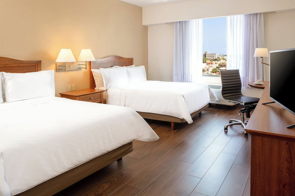 Habitació d'hotel amb dos llits, una taula amb televisió, una cadira i vistes a la ciutat.