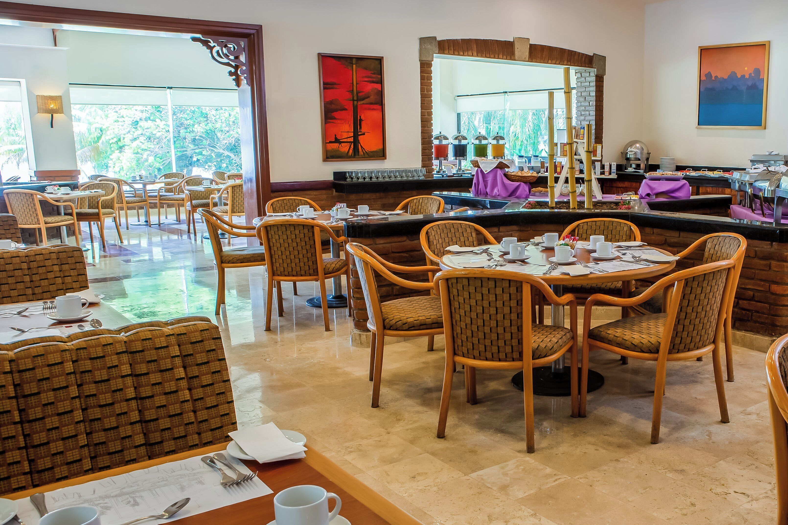A restaurant with wooden furniture, a buffet area, and large windows offering a view of greenery.