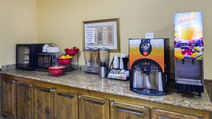 A kitchen area with a coffee maker, a juice dispenser, and various food containers.