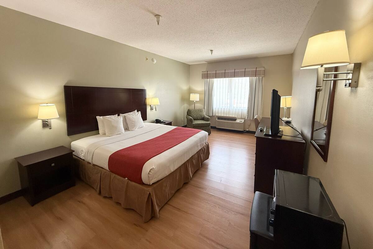 A hotel room with a large bed, bedside lamps, a TV, a chair, and a desk.