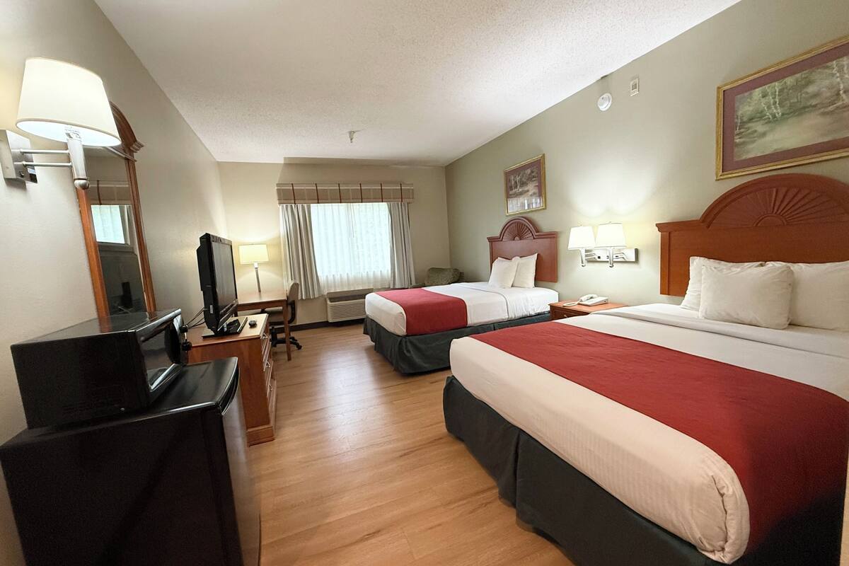 A hotel room with two beds, a desk with a computer, a TV, and a window with curtains.
