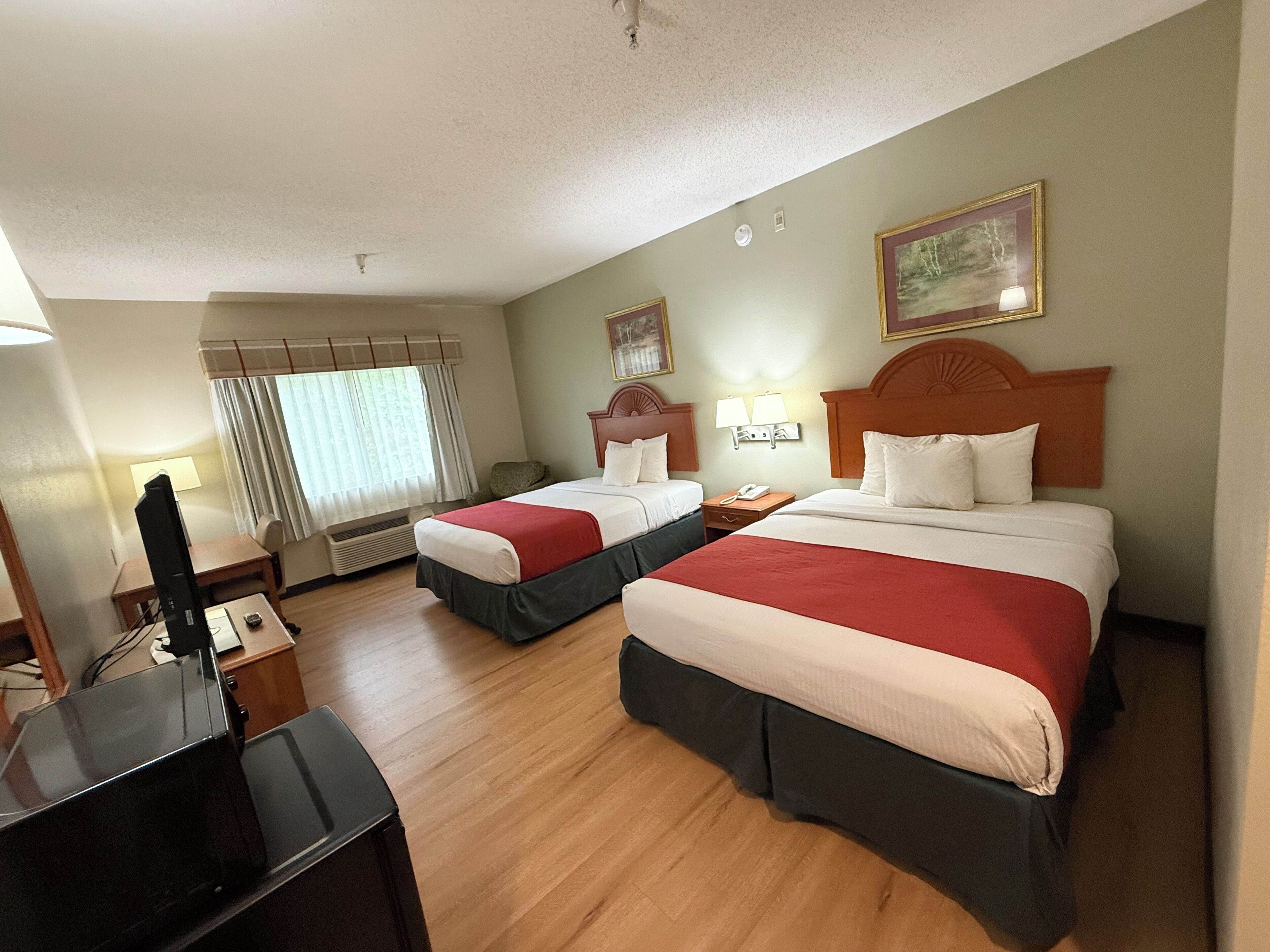A hotel room with two beds, a desk, a TV, and a window with curtains.