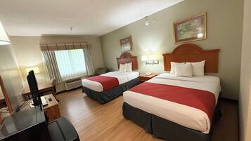 A hotel room with two beds, a desk, a TV, and a window with curtains.