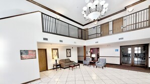 A spacious lobby with a high ceiling, a chandelier, a flag, and a staircase.