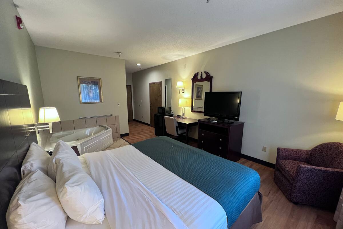 A hotel room with a large bed, a desk with a computer, a TV, and a chair.