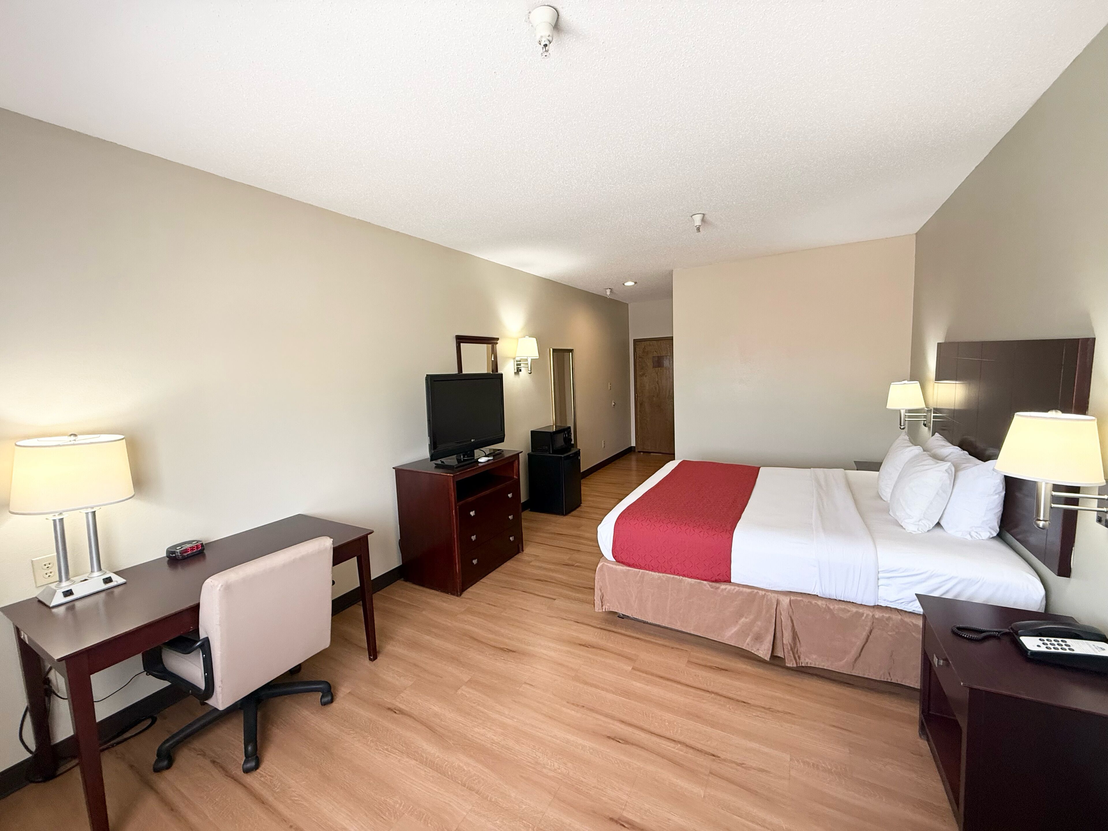 A hotel room with a bed, desk, chair, TV, and bedside lamps.