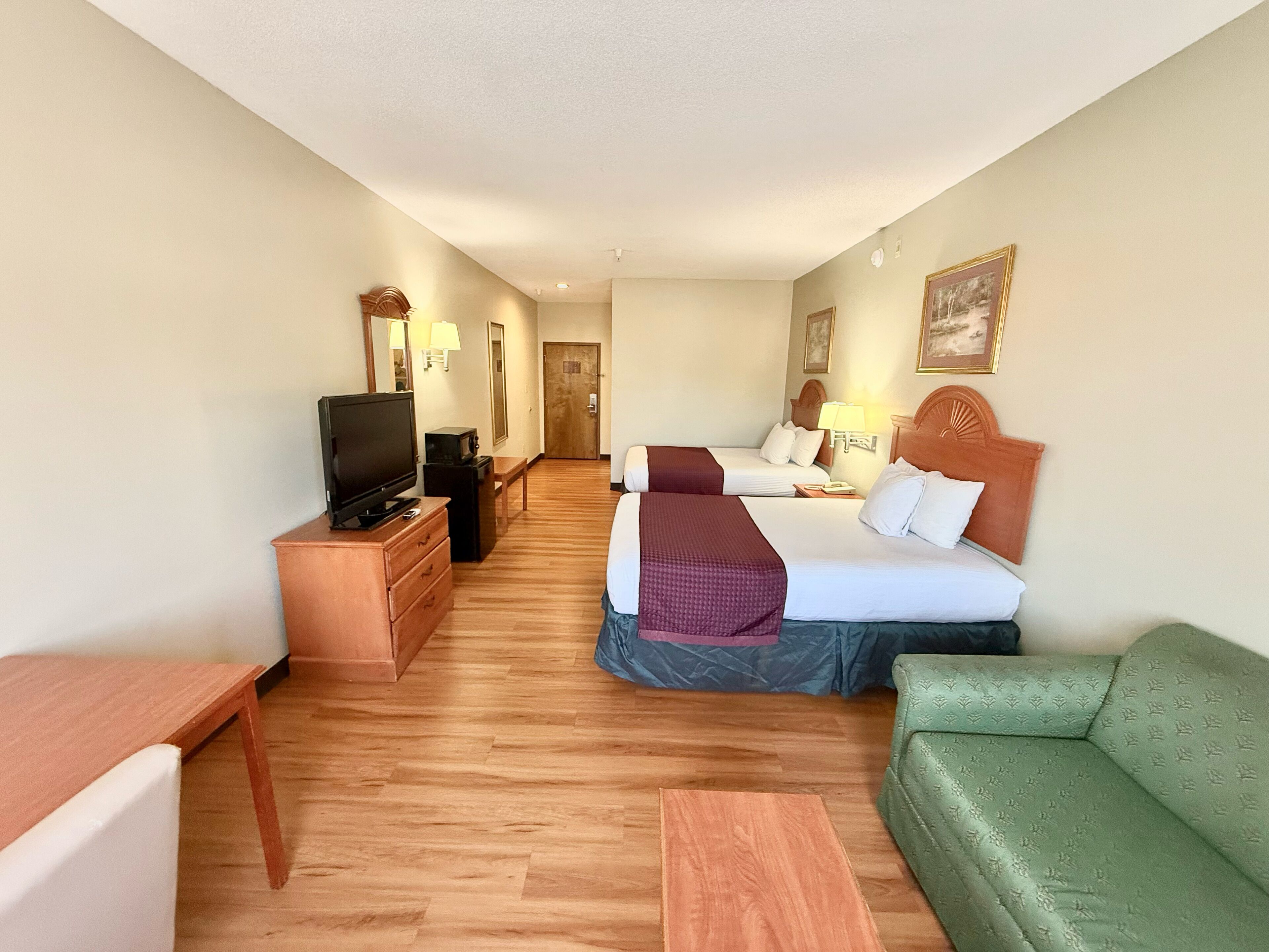 A hotel room with two beds, a television, a desk, and a green sofa.
