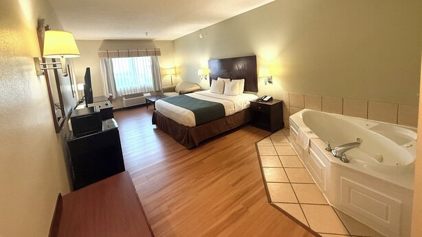 A hotel room with a bed, a desk, a chair, a desk lamp, a telephone, a television, a window with curtains, and a bathtub.