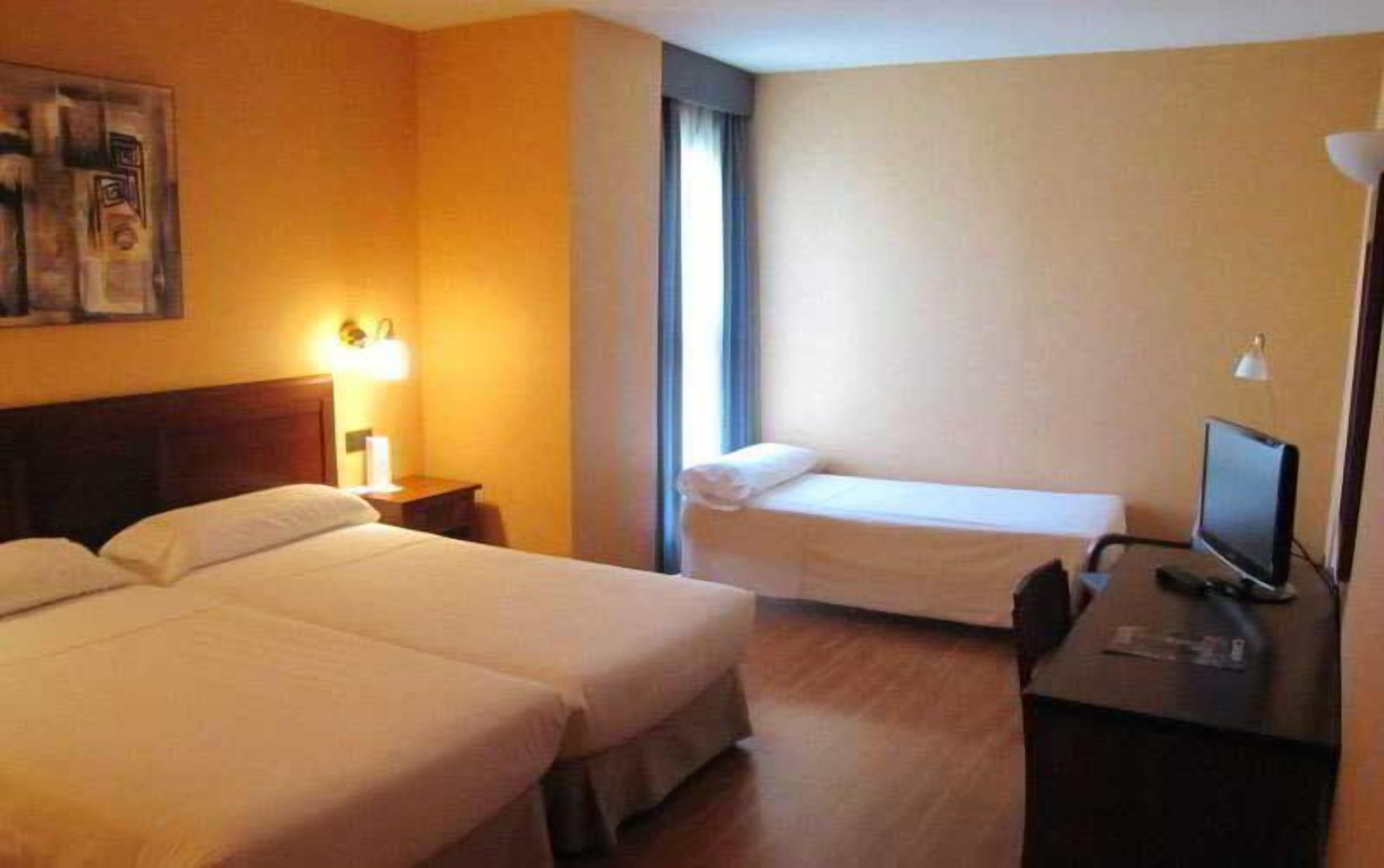A hotel room with two beds, a desk with a computer, and a window.