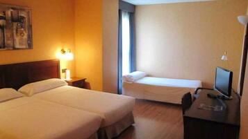 A hotel room with two beds, a desk with a computer, and a window.