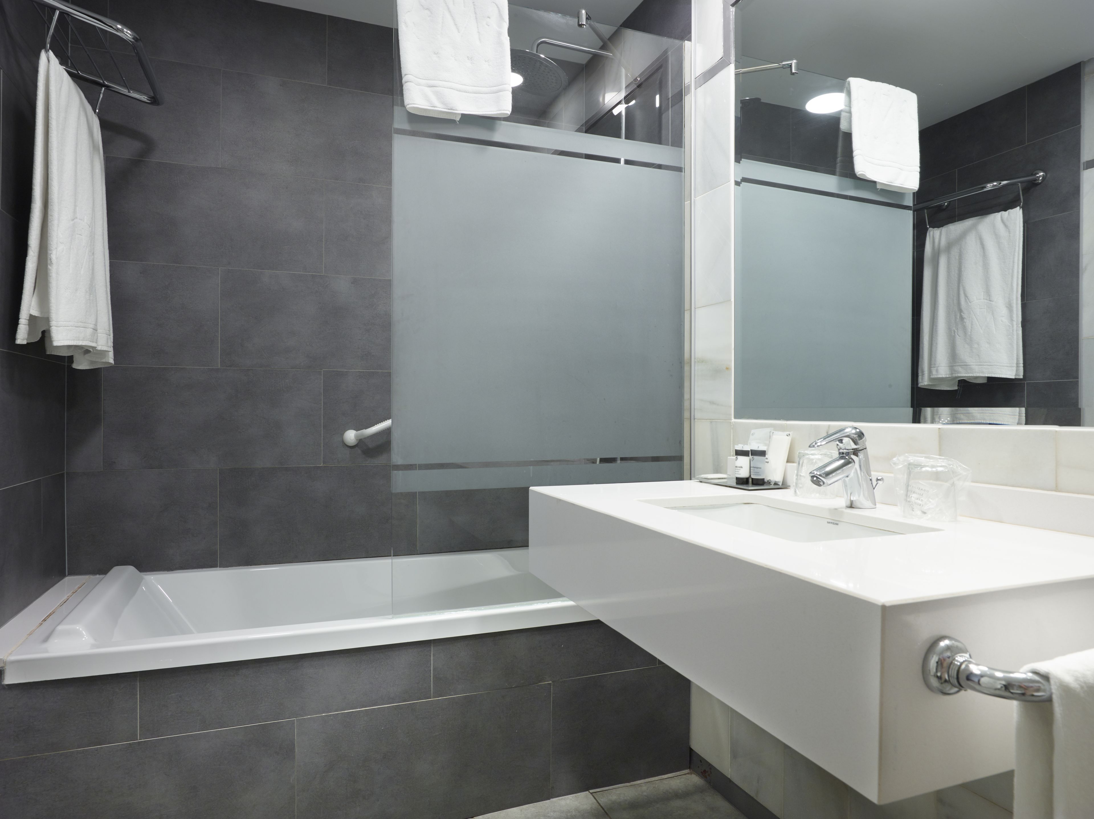 Un baño moderno con una bañera, un espejo grande y un mueble de tocador blanco.