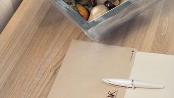 A clear glass vase with pink flowers and green leaves on a wooden table, alongside a white pen and a business card.