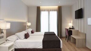 Habitación de hotel con dos camas, un escritorio, una silla, un televisor y una ventana con cortinas.