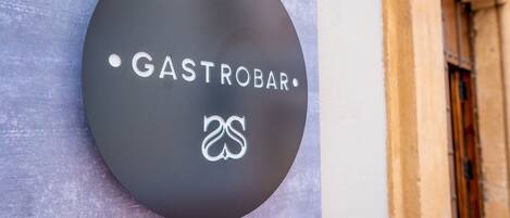 Ein rundes Schild mit dem Text "GASTROBAR" und einem Logo, an einer Wand befestigt.
