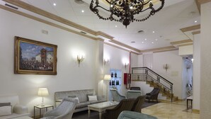Amplia sala de estar con una araña, un sofá, sillones, una mesa de centro y un cuadro en la pared.
