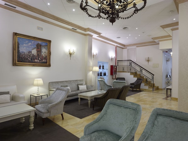 A spacious living area with a chandelier, a sofa, armchairs, a coffee table, and a painting on the wall. - Hotel Maestranza (Ronda)